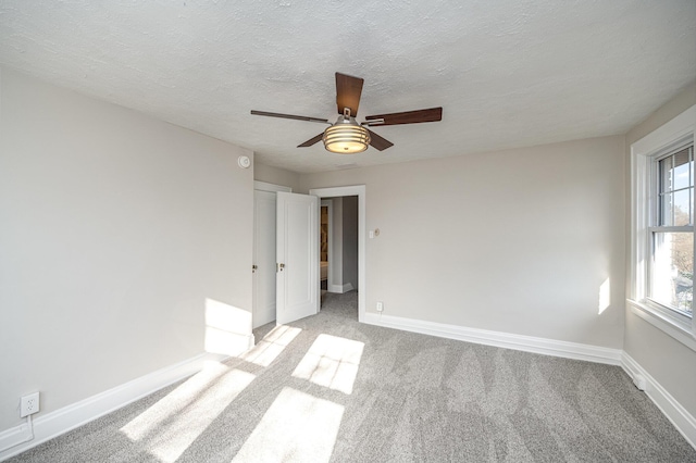 unfurnished bedroom featuring light carpet, ceiling fan, a textured ceiling, and baseboards