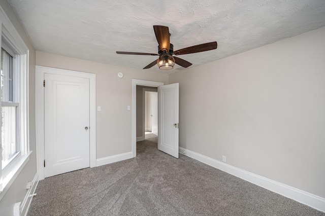 unfurnished bedroom featuring carpet flooring, a textured ceiling, baseboards, and a ceiling fan