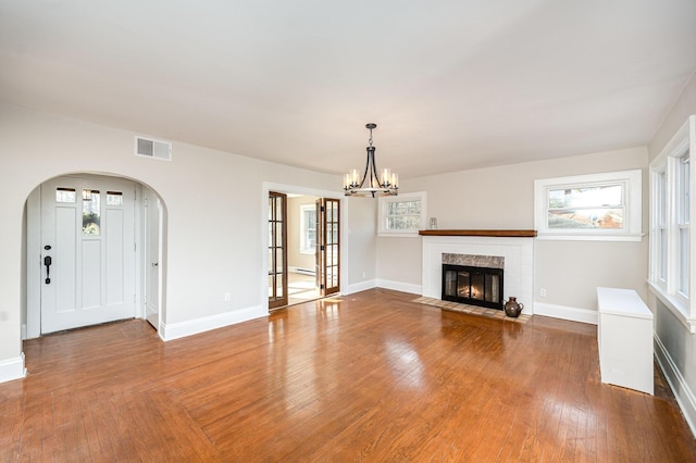 unfurnished living room featuring visible vents, arched walkways, a notable chandelier, and light wood-style flooring