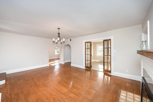 unfurnished living room with baseboards, arched walkways, visible vents, and light wood finished floors