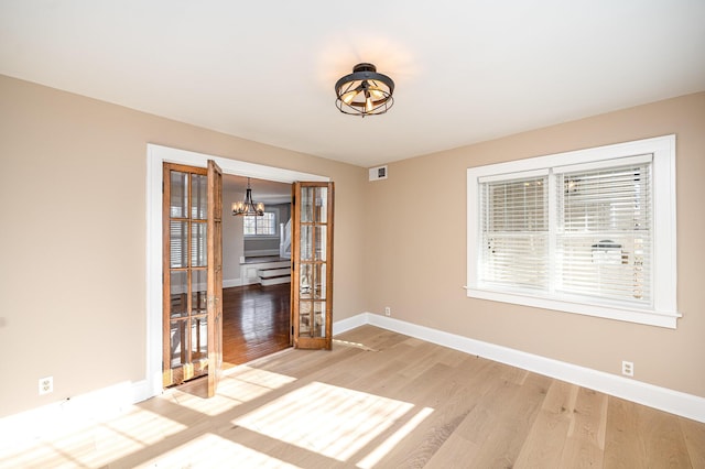 spare room with light wood-type flooring, baseboards, a notable chandelier, and visible vents