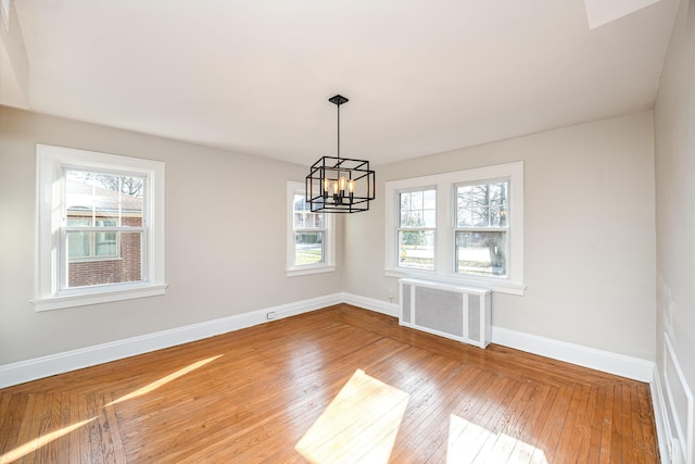 unfurnished room featuring hardwood / wood-style floors, baseboards, radiator, and a chandelier