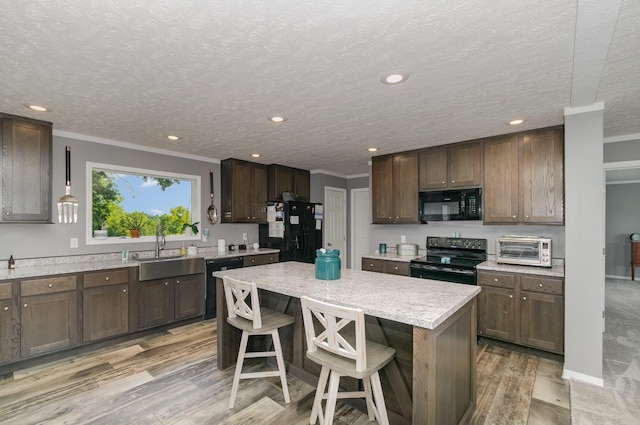 kitchen featuring light wood finished floors, ornamental molding, a sink, black appliances, and a center island