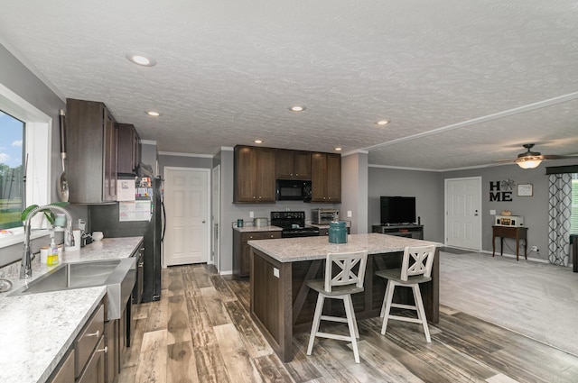 kitchen featuring black appliances, ornamental molding, a kitchen breakfast bar, a kitchen island, and dark brown cabinets