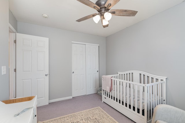 carpeted bedroom with a nursery area, baseboards, a closet, and ceiling fan