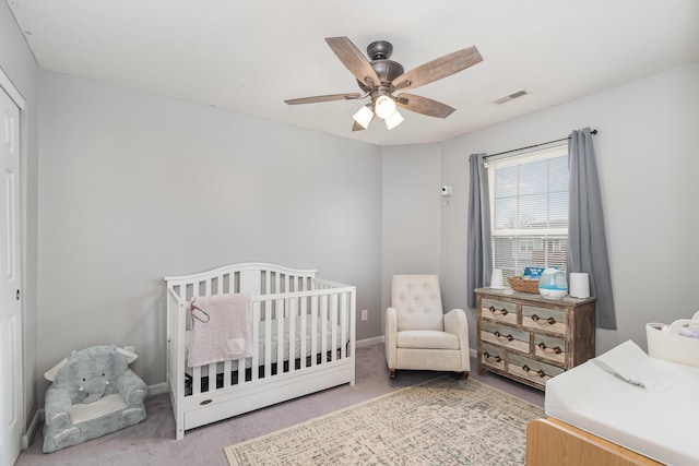 carpeted bedroom with visible vents, a crib, baseboards, and a ceiling fan