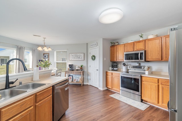 kitchen featuring a sink, appliances with stainless steel finishes, light countertops, a chandelier, and dark wood-style flooring