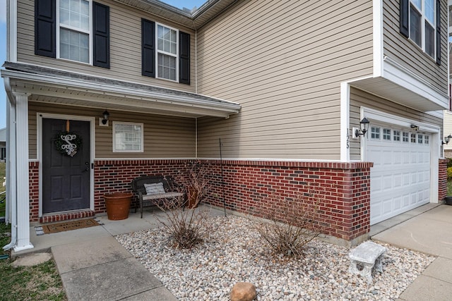 view of exterior entry with a garage, brick siding, and driveway