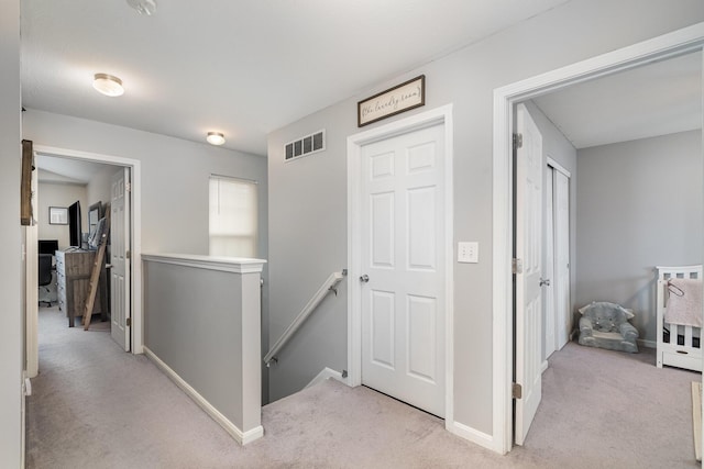 hall featuring light colored carpet, an upstairs landing, visible vents, and baseboards