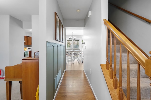 hallway featuring a chandelier, light wood-style flooring, stairs, and baseboards