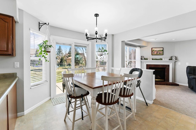 dining room featuring baseboards, light colored carpet, a brick fireplace, and a chandelier