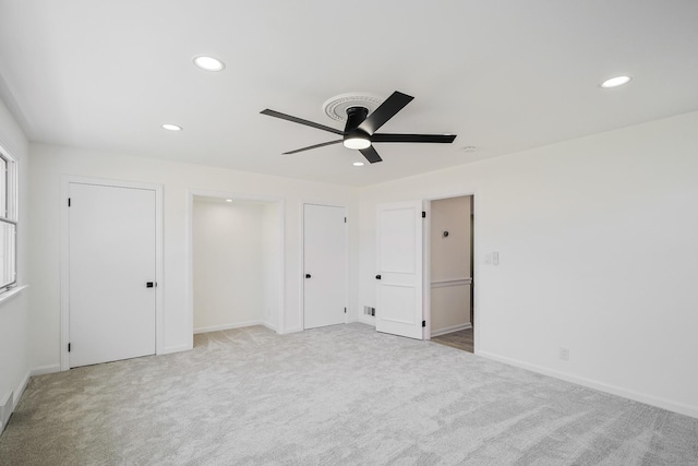 unfurnished bedroom featuring light carpet, two closets, recessed lighting, baseboards, and ceiling fan