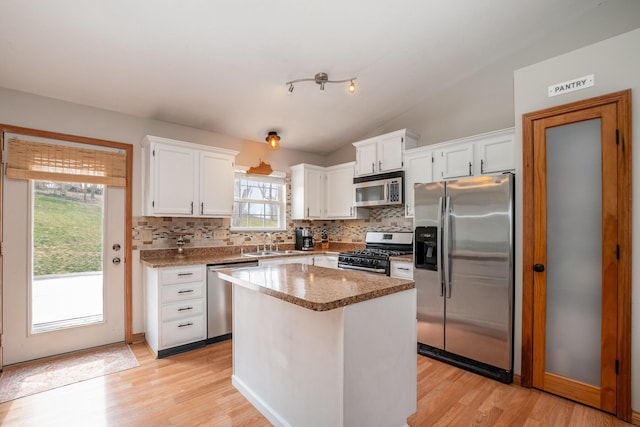 kitchen featuring a sink, stainless steel appliances, white cabinets, tasteful backsplash, and a center island