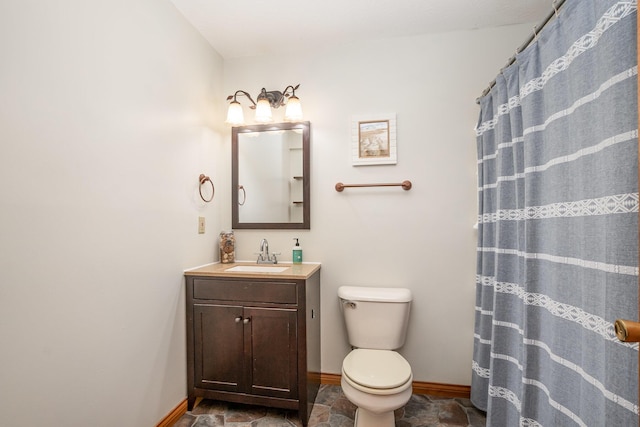 bathroom featuring stone finish floor, toilet, vanity, and baseboards