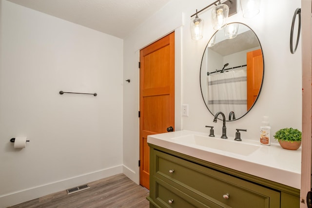 full bath with visible vents, vanity, baseboards, and wood finished floors