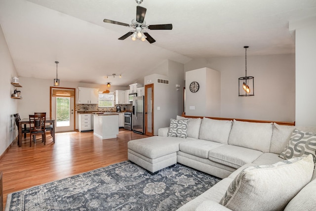 living room with visible vents, ceiling fan, vaulted ceiling, and light wood-style flooring