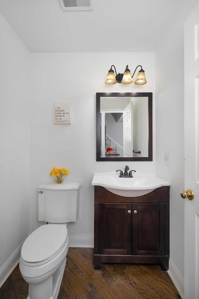 half bathroom featuring visible vents, baseboards, toilet, wood finished floors, and vanity