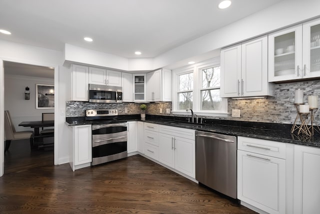 kitchen featuring decorative backsplash, glass insert cabinets, appliances with stainless steel finishes, and a sink