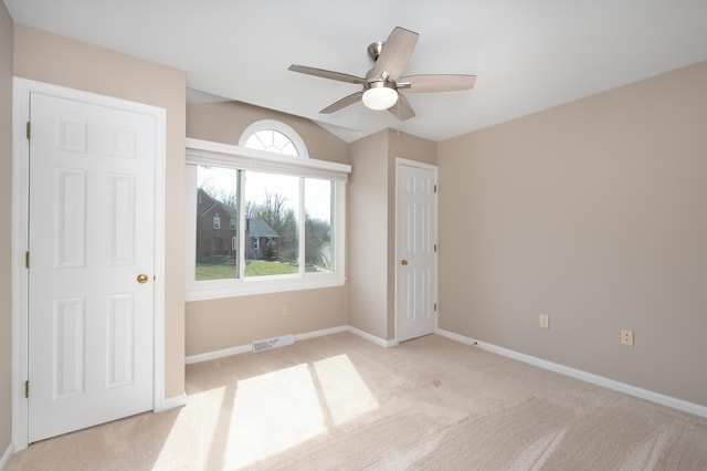 unfurnished bedroom featuring visible vents, baseboards, lofted ceiling, light carpet, and a ceiling fan