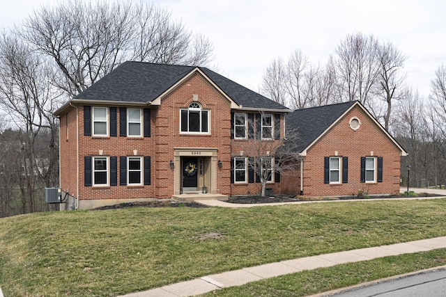 colonial inspired home featuring cooling unit, brick siding, and a front yard