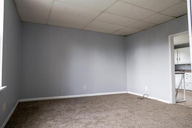 carpeted empty room featuring a paneled ceiling and baseboards