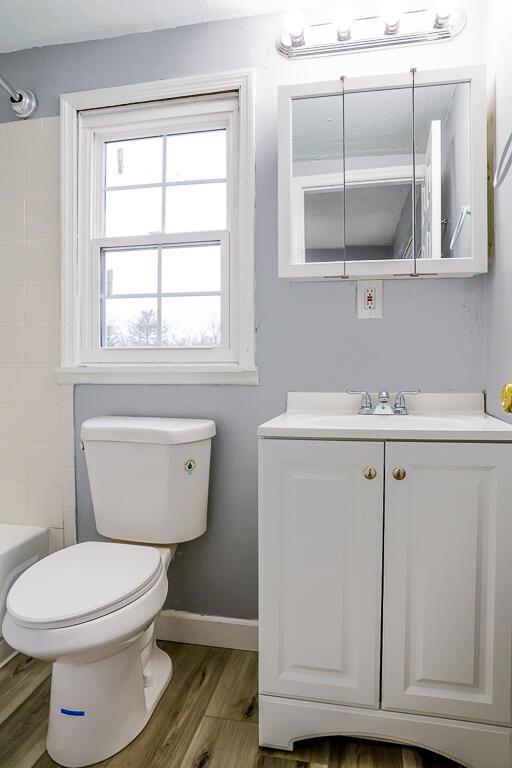 full bath featuring vanity, wood finished floors, baseboards, shower / washtub combination, and toilet