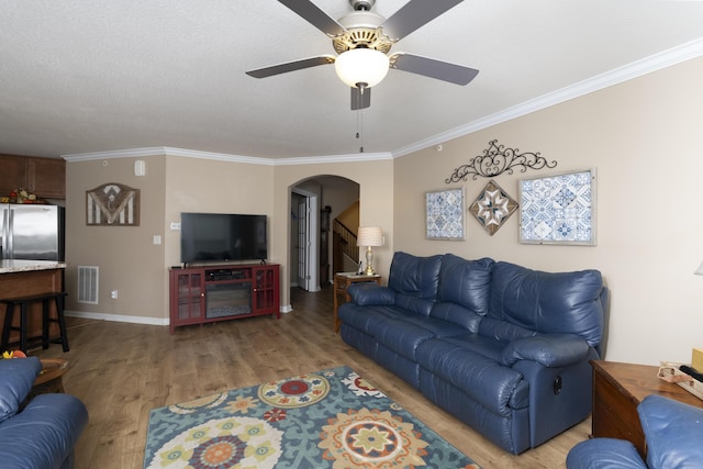 living area with a ceiling fan, visible vents, arched walkways, ornamental molding, and light wood-type flooring