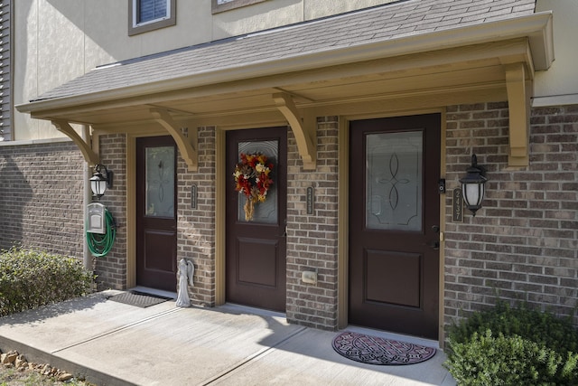 doorway to property featuring brick siding, covered porch, and a shingled roof