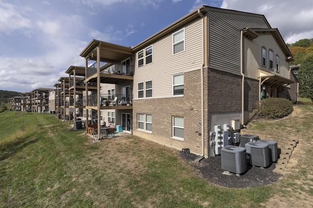 back of property with brick siding, a lawn, and central AC