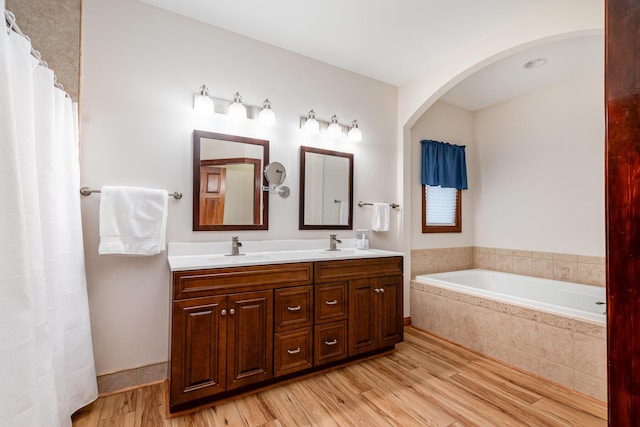 bathroom with double vanity, a sink, a bath, and wood finished floors
