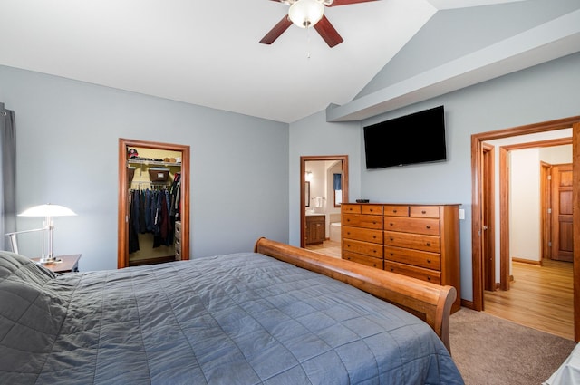 bedroom with vaulted ceiling, light carpet, a walk in closet, ensuite bath, and ceiling fan