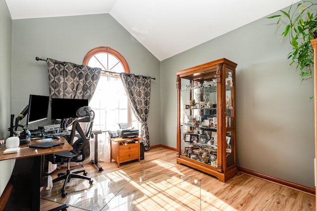 office area with baseboards, light wood-style floors, and vaulted ceiling