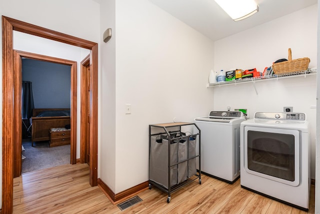 washroom with washing machine and dryer, laundry area, baseboards, visible vents, and light wood-style floors