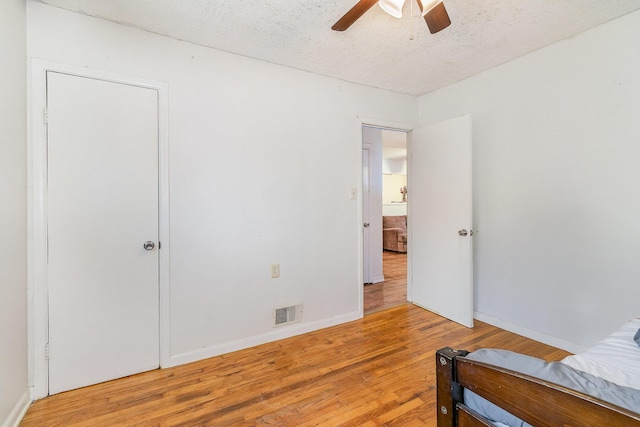 bedroom featuring a textured ceiling, visible vents, baseboards, ceiling fan, and wood finished floors