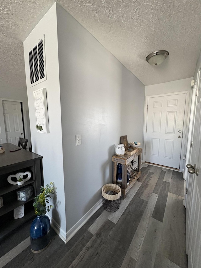 corridor with baseboards, wood finished floors, and a textured ceiling
