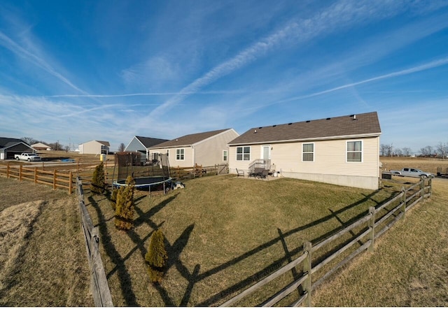 rear view of property with a trampoline, a yard, a patio, and fence