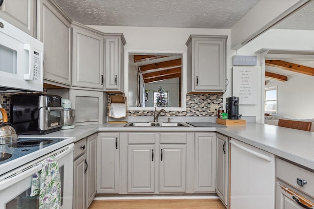kitchen featuring white appliances, gray cabinets, light countertops, and a sink