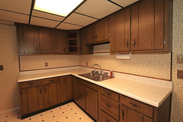 kitchen featuring wallpapered walls, a drop ceiling, light floors, light countertops, and a sink