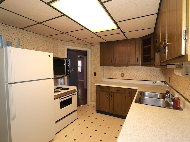 kitchen with wallpapered walls, light floors, light countertops, a sink, and white appliances