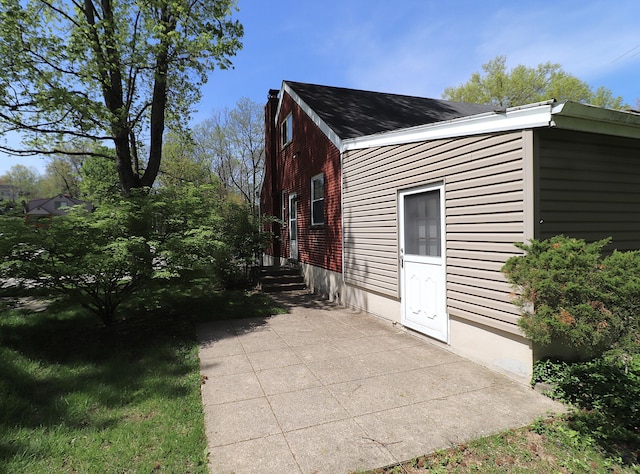 view of home's exterior featuring a chimney, roof with shingles, and a patio area