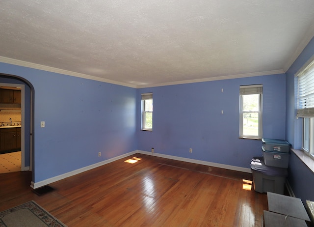 unfurnished room featuring crown molding, a sink, wood-type flooring, baseboards, and visible vents