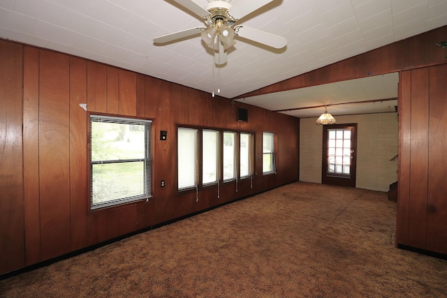 unfurnished living room with vaulted ceiling, carpet, wood walls, and ceiling fan