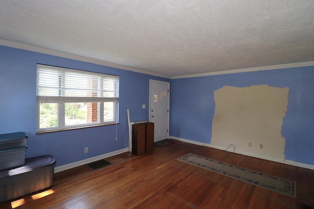 empty room featuring wood finished floors, a textured ceiling, baseboards, ornamental molding, and visible vents