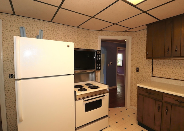 kitchen with wallpapered walls, white appliances, light tile patterned floors, light countertops, and a paneled ceiling