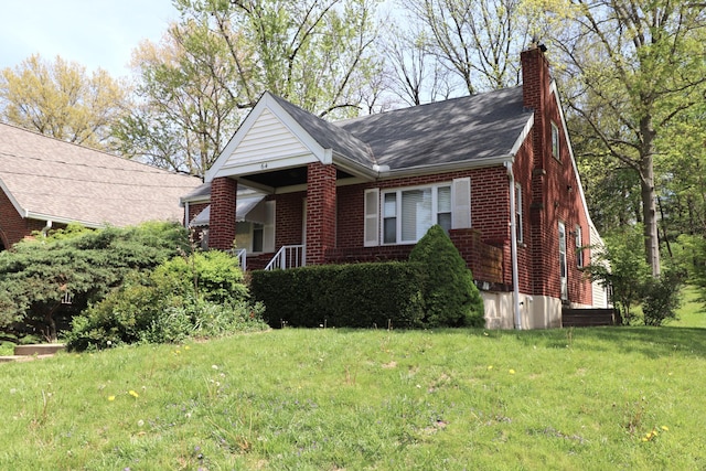view of front of home featuring a shingled roof, a chimney, brick siding, and a front yard