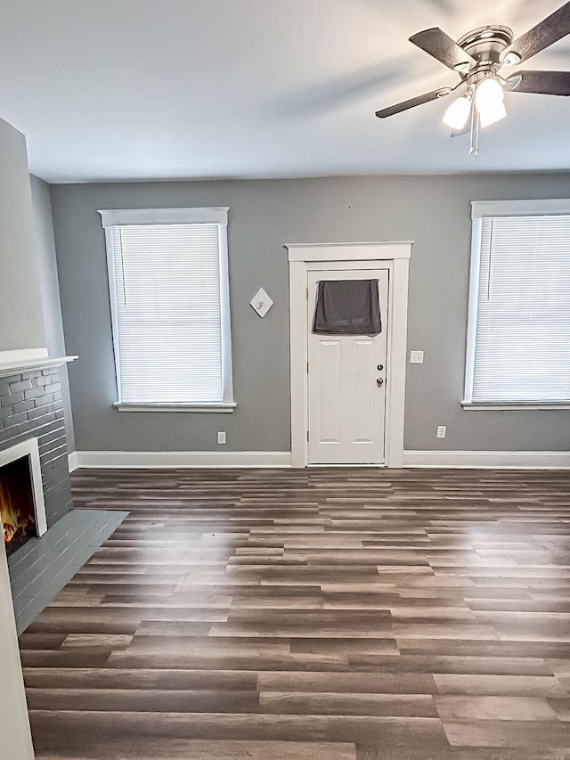 unfurnished living room with wood finished floors, baseboards, and a brick fireplace