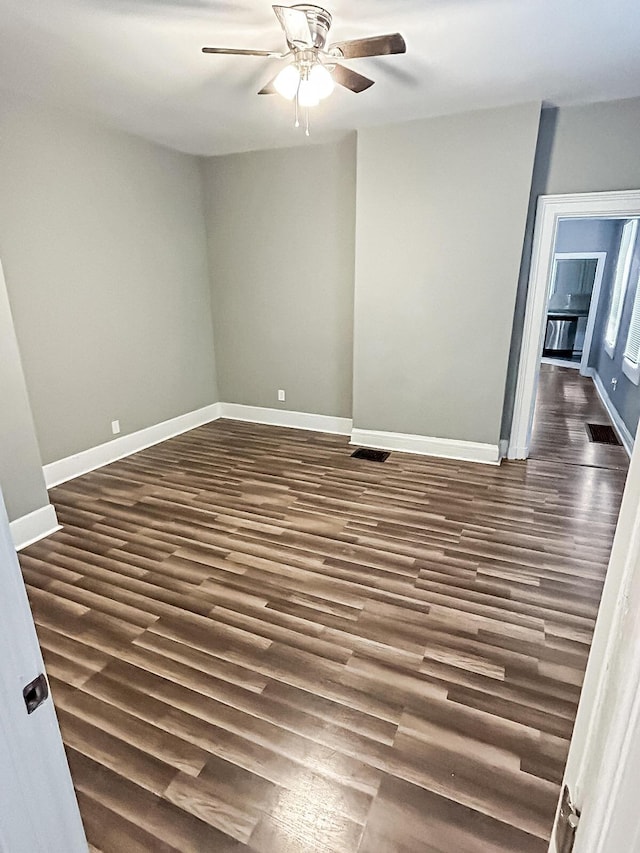 empty room featuring dark wood-style flooring, baseboards, visible vents, and ceiling fan