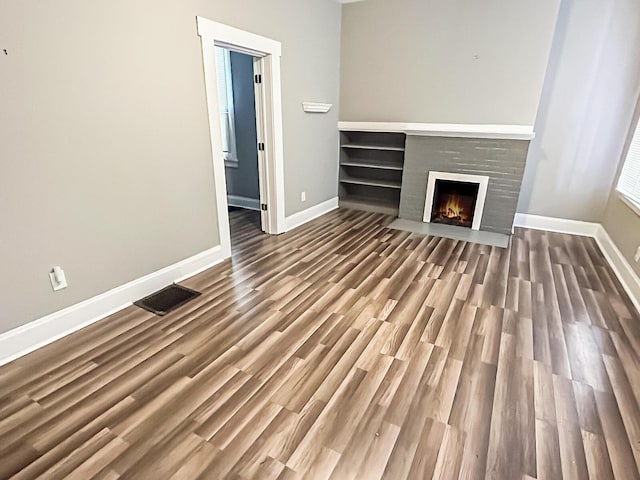 unfurnished living room with visible vents, a lit fireplace, baseboards, and wood finished floors