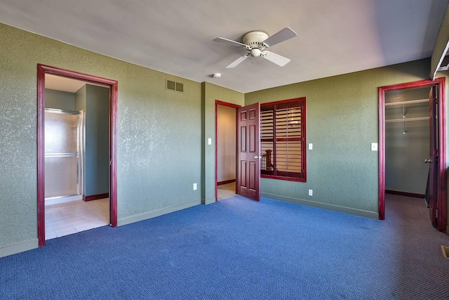 unfurnished bedroom featuring carpet flooring, visible vents, a spacious closet, a textured wall, and ensuite bath
