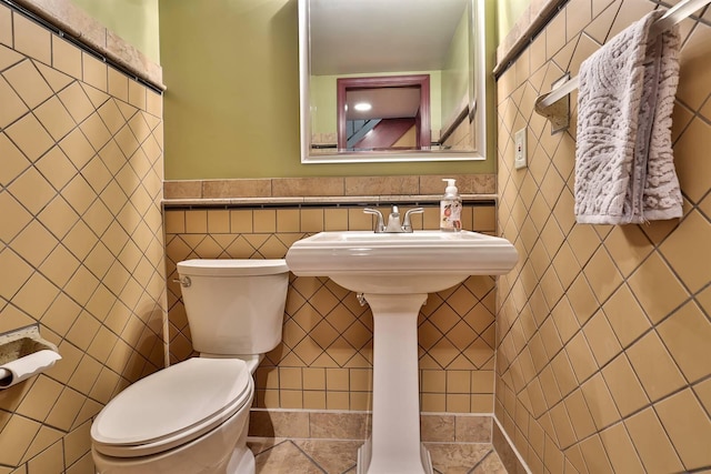 half bath featuring tile walls, toilet, and wainscoting
